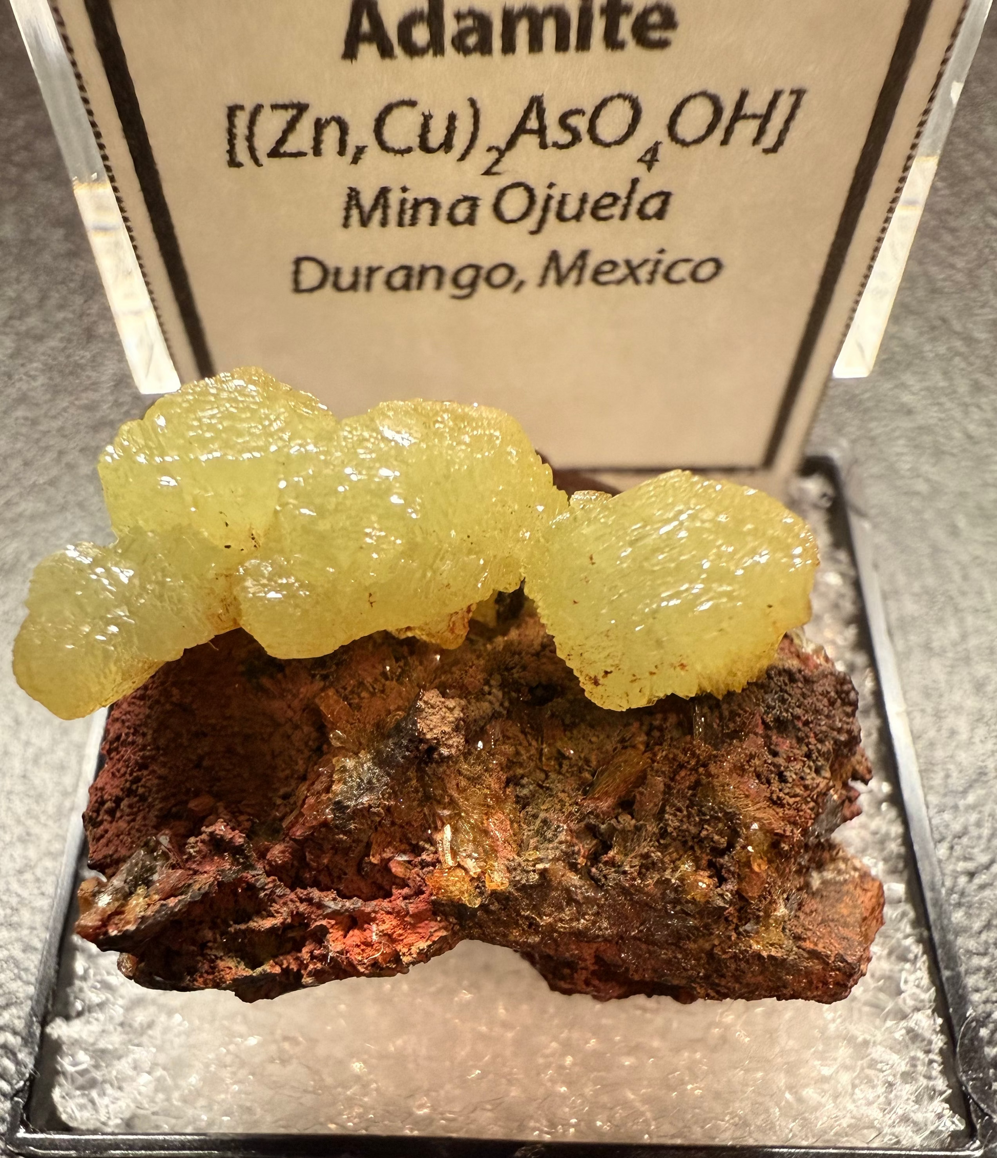 Mineral sample of Adamite with a label on a dark surface