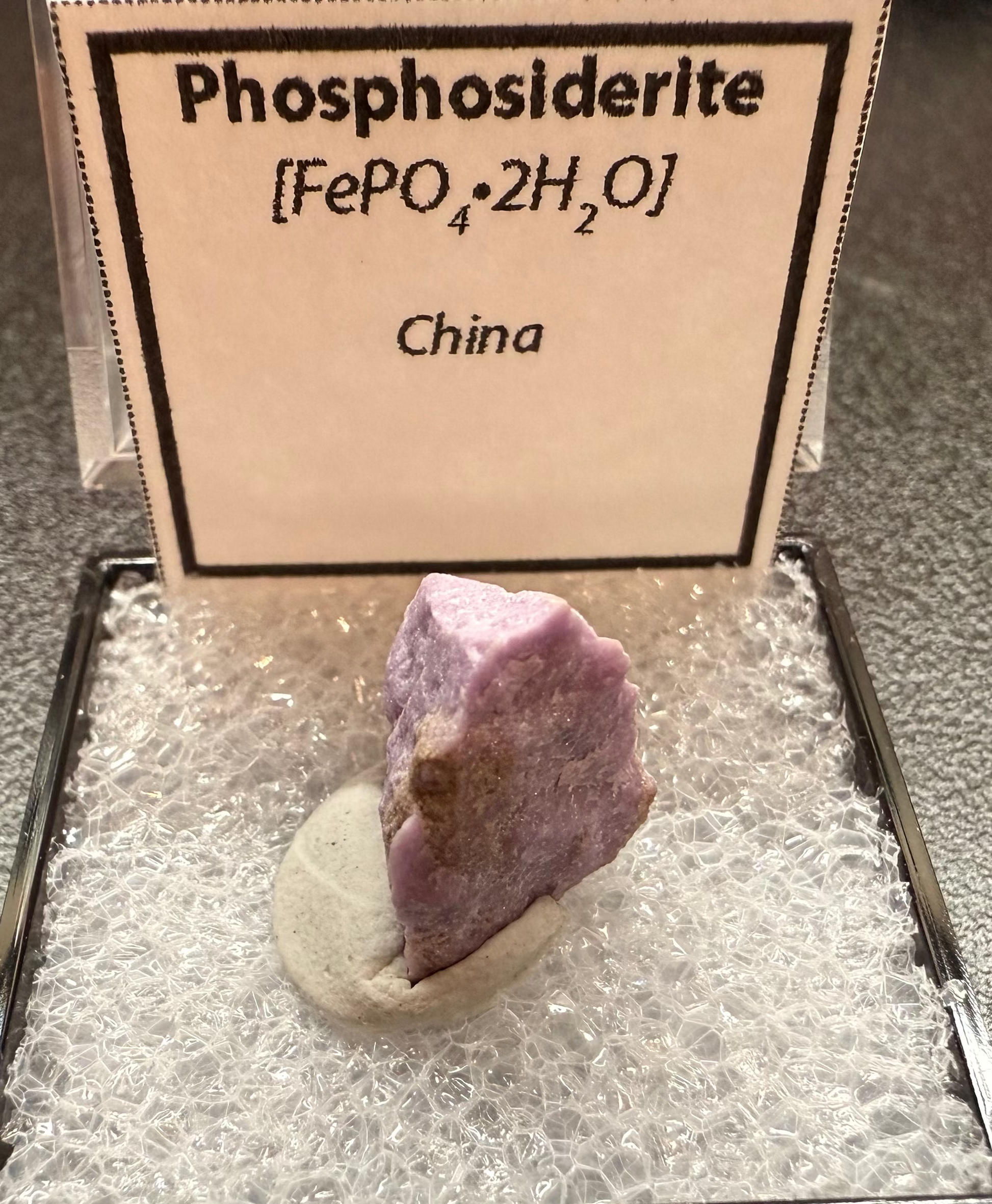 Phosphosiderite mineral specimen in a display case with a label on a dark surface