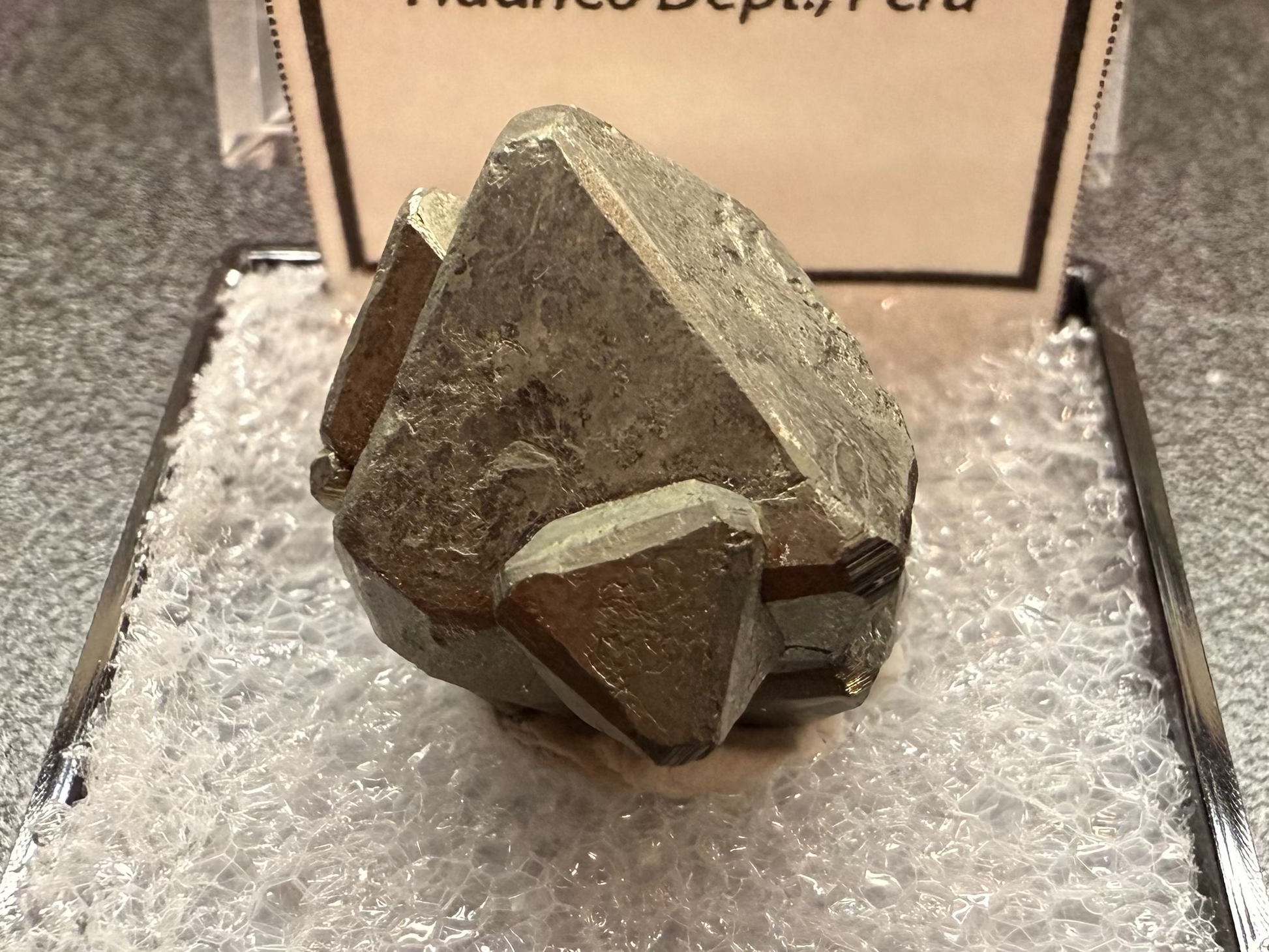 Pyrite octahedron crystal on a stand with a label indicating its origin.