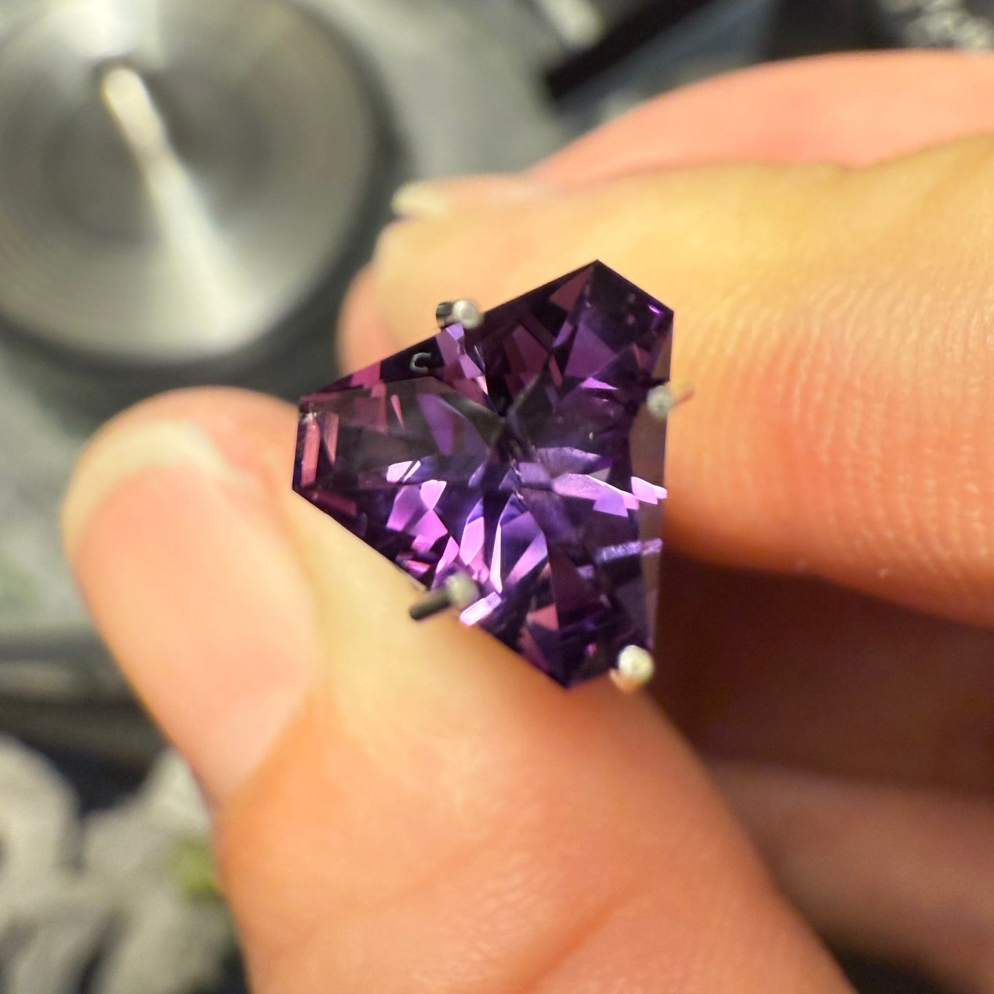 Purple gemstone held between fingers with a blurred background